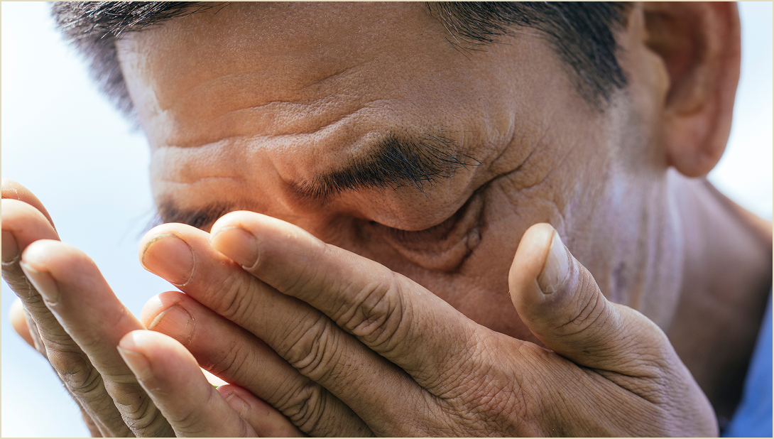 A man inhaling the scent of the tea leaves in his palms.